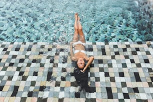 Woman relaxing in luxury swimming pool in white bikini