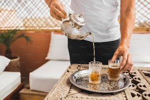 銀のビンテージティーポットを手に持ち、伝統的なミントの甘いモロッコのお茶を注ぐ男性。アラビアのおもてなしとサービス。