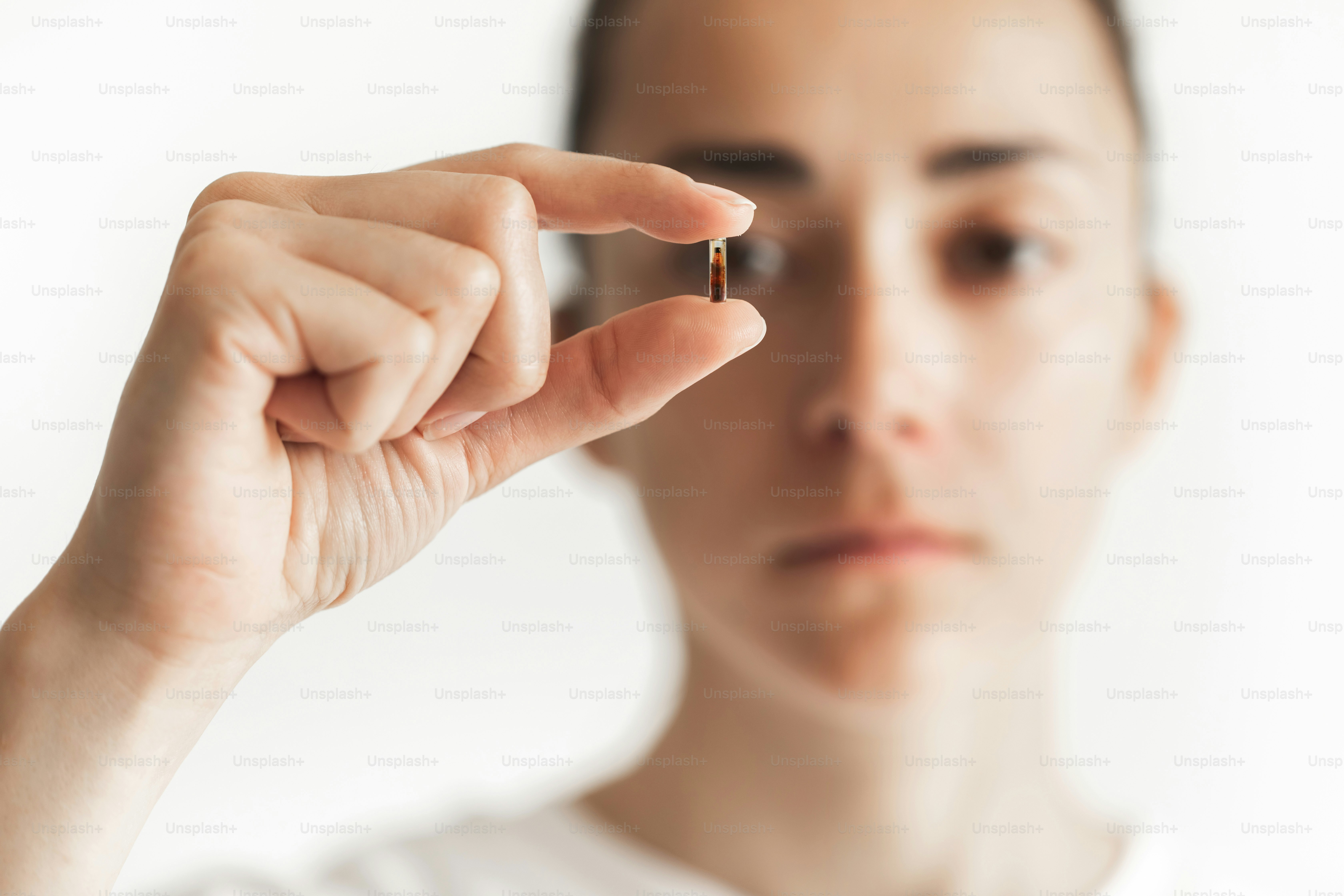 Person, die in den Fingern einen Mikrochip für die Implantation mit defokussiertem Gesicht auf dem Hintergrund hält. Zukünftige obligatorische Chipisierung von Menschen. Staatliche Kontrolle.