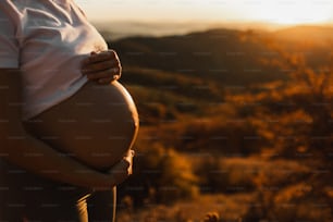 Woman hands hold belly  in pregnancy outdoors closeup. Amazing warm sunset light. Maternity and childbirth concept.