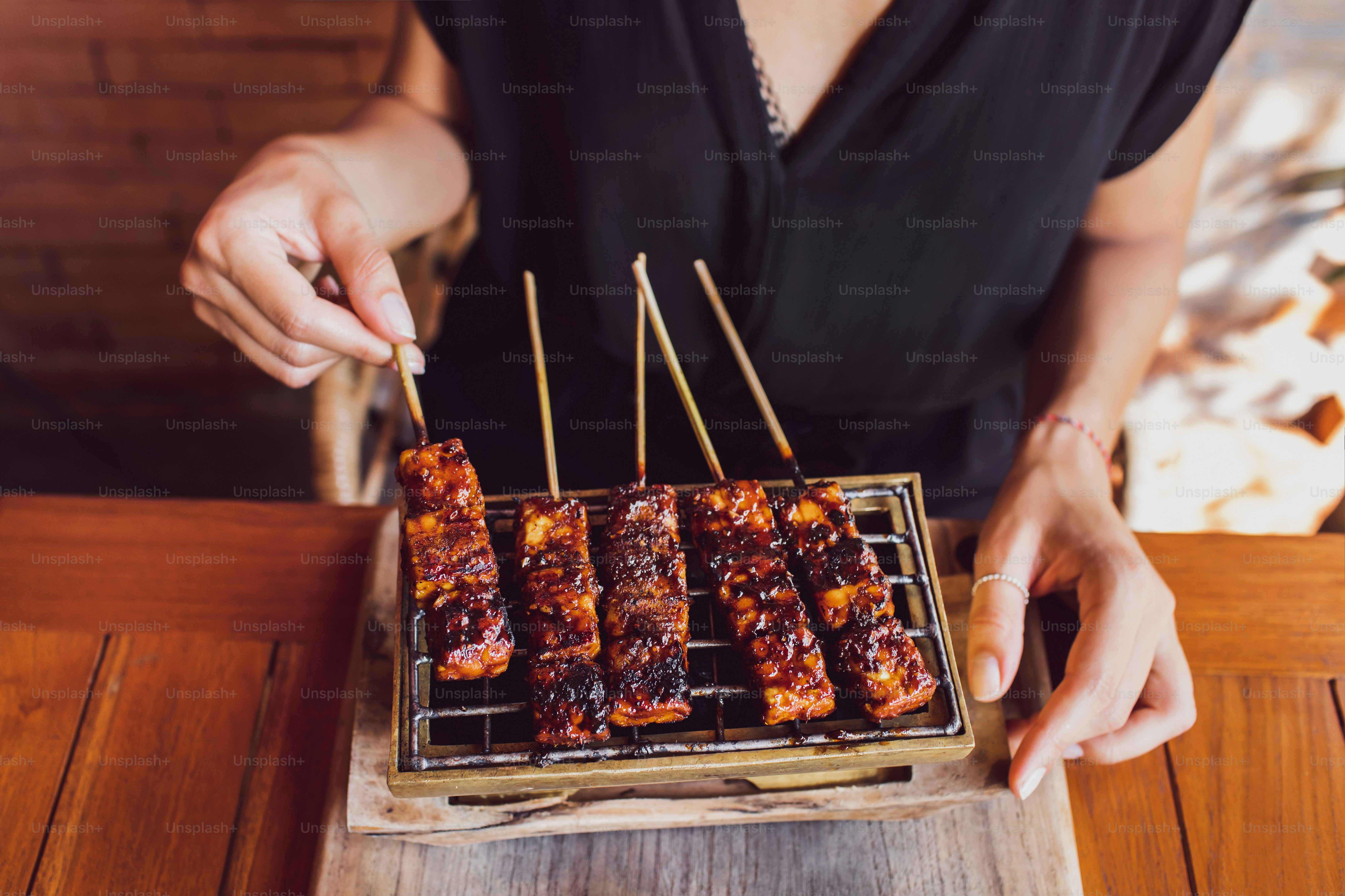 Woman is holding traditional indonesian grilled skewers of tempe. Vegan food concept. Top view.