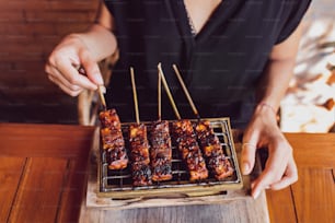 Woman is holding traditional indonesian grilled skewers of tempe. Vegan food concept. Top view.