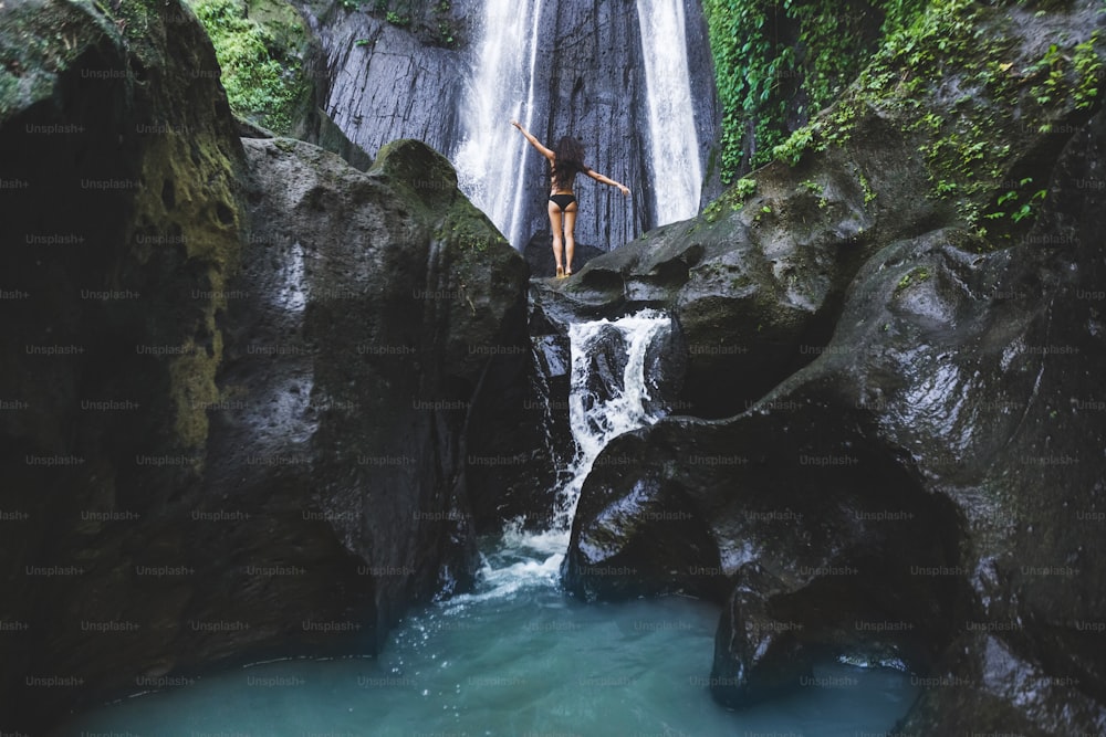 Donna che gode vicino nascosto nella cascata della giungla a Bali. Corpo snello e costume da bagno nero, modello di moda. Dusun Kuning nella zona di Ubud