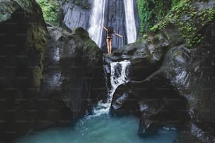 Frau genießt in der Nähe versteckt im Dschungel Kaskaden-Wasserfall in Bali. Schlanker Körper und schwarzer Badeanzug, Model. Dusun Kuning in der Umgebung von Ubud