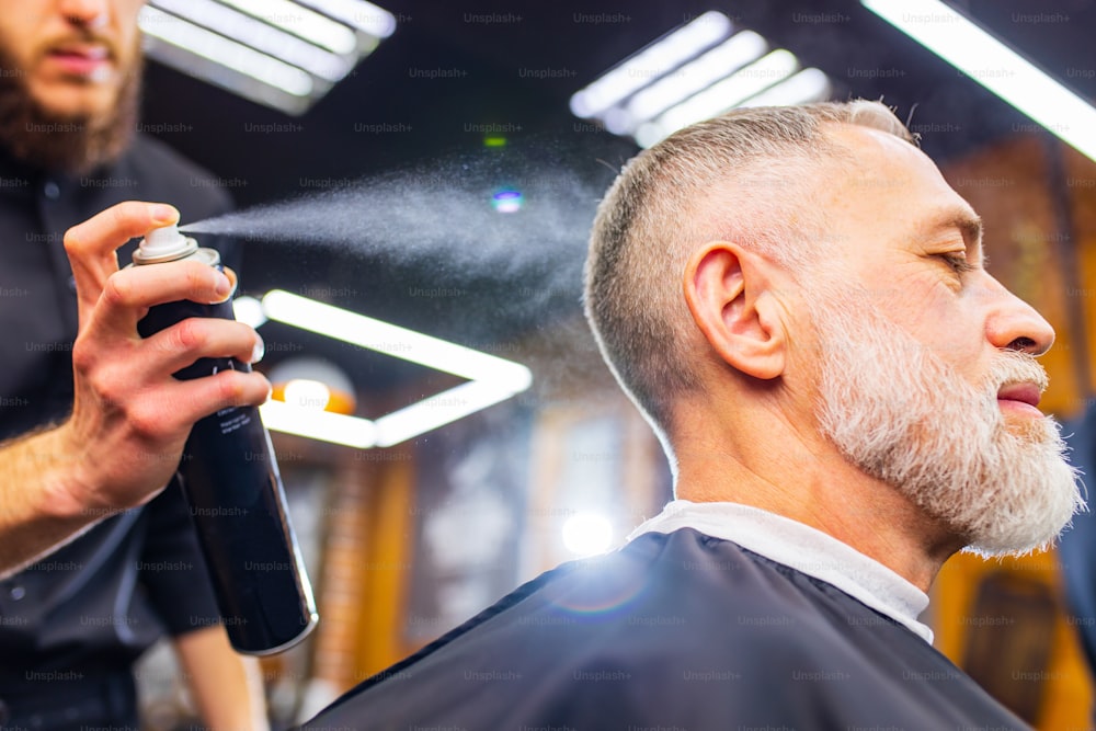 現代の理髪店でヘアスタイリストを訪問する年配のハンサムな男性。
