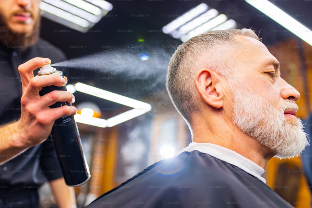 Senior handsome man visiting hairstylist in modern barber shop.