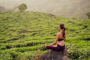 donna in stoffa viola che fa yoga nelle piantagioni di tè nella collina di Munnar Kerala India.