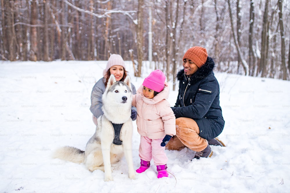 Hombre afro con su esposa caucásica divirtiéndose con una hermosa hija jugando husky en un parque nevado.