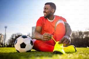 Heureux joueur de football hispanique multiculturel souriant et portant un costume sportif rouge en plein air ensoleillé.