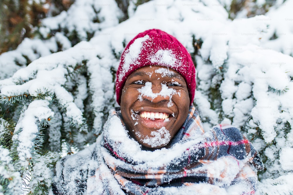 Hombre hispano con sombrero rojo con copo de nieve en la cara divirtiéndose y sintiendo el estado de ánimo navideño en el parque.