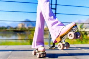 멋진 땋은 머리, 흰색 티셔츠, 플레어 핑크 바지를 입은 아름다운 금발 십대 소녀의 초상화는 공원에서 롤러를 타고 스케이트를 탄다.