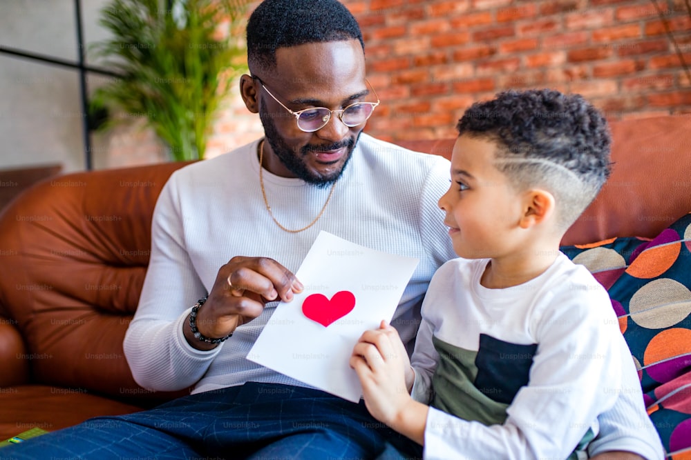 bambino afroamericano che regala al papà una foto di San Valentino in salotto.