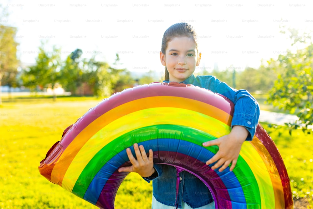Bella ragazza di sette anni ispanica latina con il grande palloncino arcobaleno all'aperto nel parco estivo.