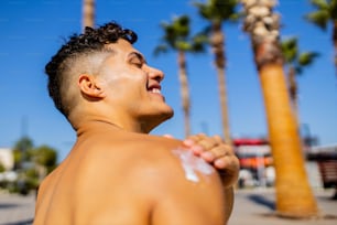 Homme brésilien fort avec un corps en cuir utilisant de la crème spf par journée ensoleillée à la plage.