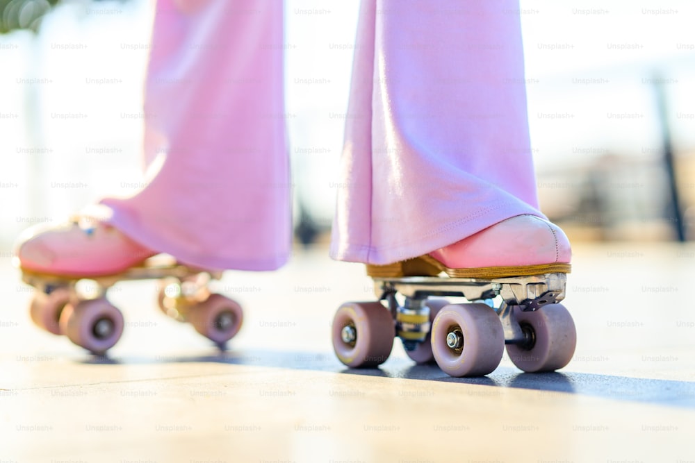 晴れた日に屋外でピンクのパステルカラーのローラースケートをしたベルボトムのズボンを着た脚の女性の接写。