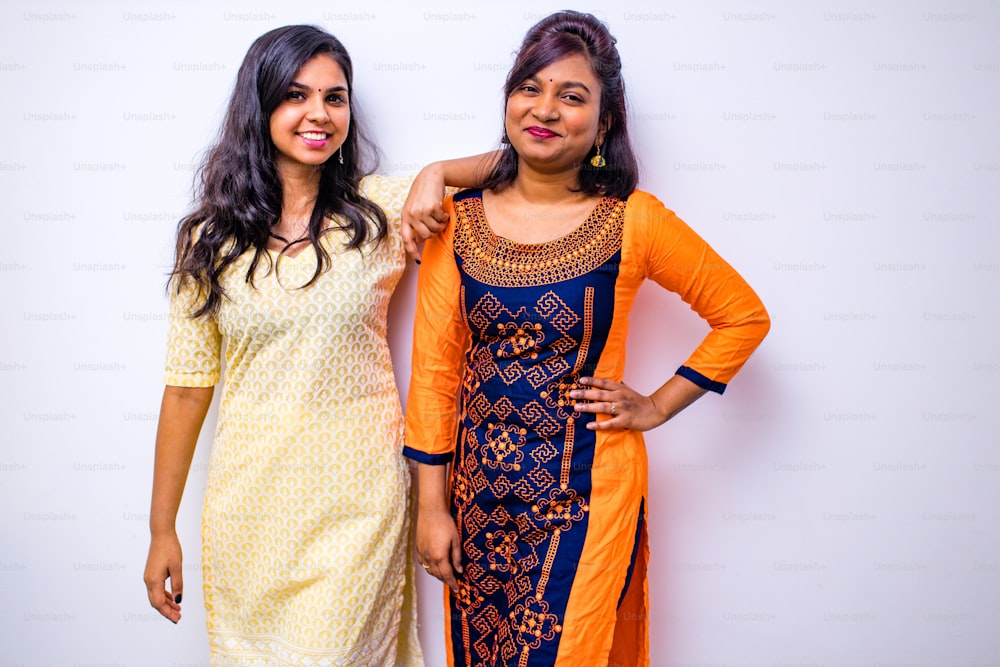 カジュアルなインドの服、白い壁の上にポーズをとるクルタの2人のインド人女性。