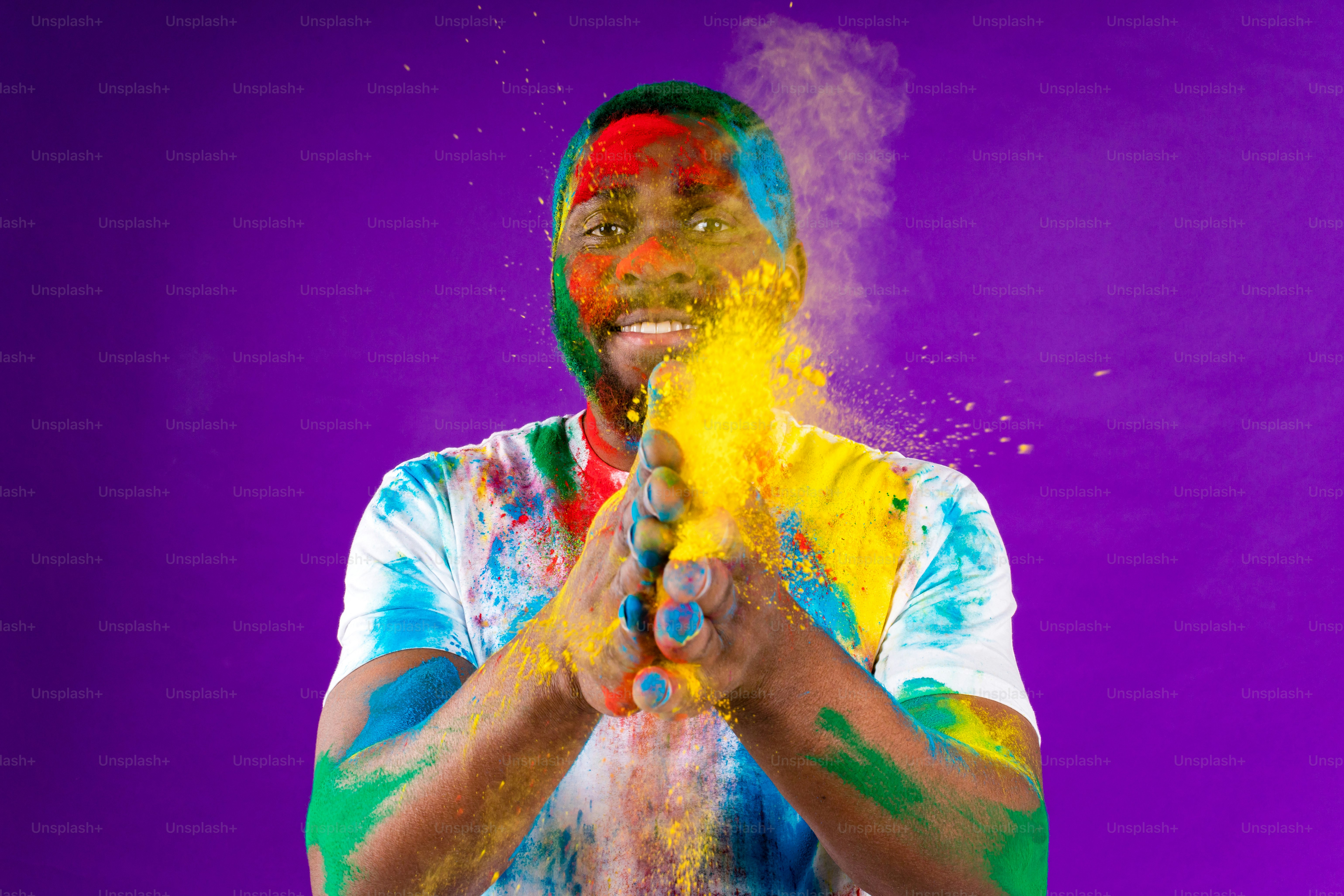 Hombre afroamericano celebra el festival holi en un estudio violeta de fondo.
