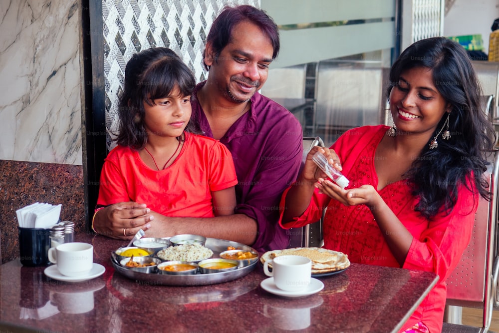 インドのカフェで食べる前に手指消毒ジェルを洗う父、母、少女。