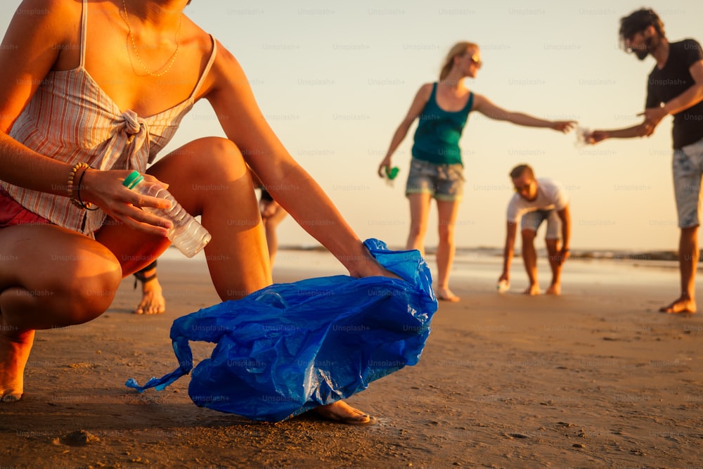 concentrarsi sulla ragazza allegra che pulisce la spiaggia sabbiosa dalla spazzatura con i suoi amici sul team di volontari di sfondo sul movimento eco-compatibile a Goa in India.