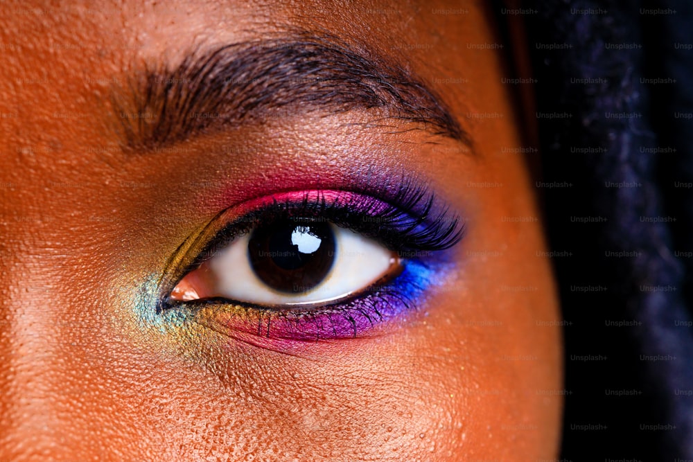 青いスタジオのバクラグラウンドに虹色の化粧と長いまつげを持つ女性。