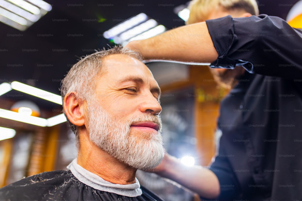 Homme à la retraite visitant le salon de coiffure, assis dans le fauteuil du coiffeur tout en obtenant une coiffure cool.