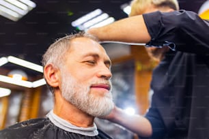Hombre jubilado visitando barbería, sentado en la silla del barbero mientras se pone peinado fresco.
