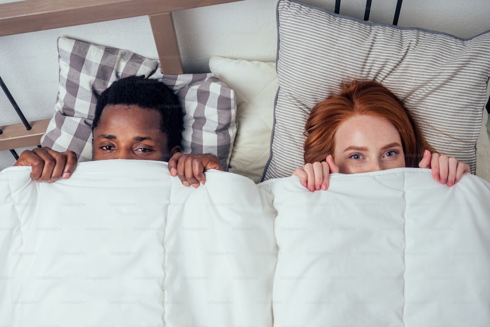roux gingembre caucasien femme heureuse et homme afro multiethnique allongé ensemble dans la chambre à coucher caché sous le concept de couverture.timidité.