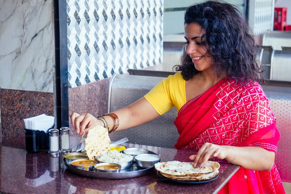 hermosa mujer morena en sari rojo comiendo con apetito tradicional thali wirh rise, cuajada, dal en Goa restaurante masala té.