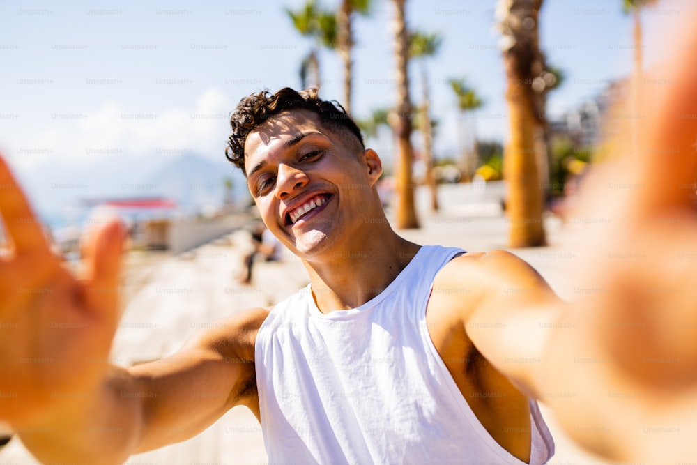 Lateinischer Mann, der ein Selfie-Porträt vor der Kamera auf See mit Palmenhintergrund macht.