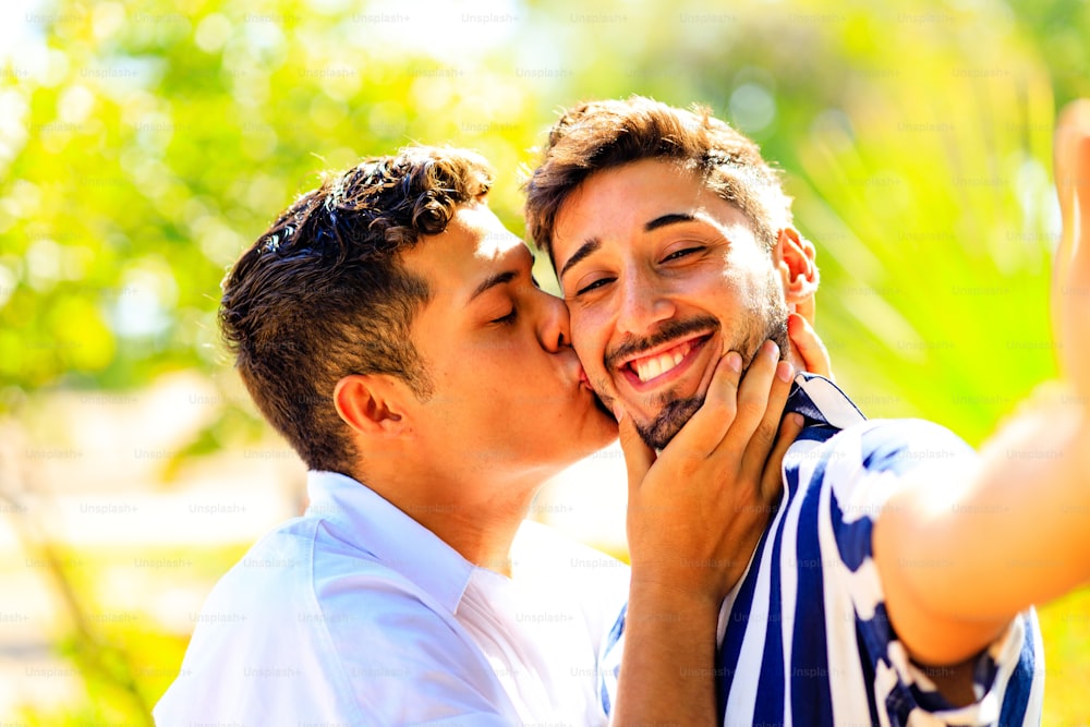 Glückliches schwules Paar, das ein Selfie mit der Handykamera im Sommerpark macht.