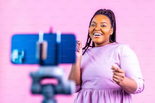 검은 피부의 여성이 웃으며 분홍색 벽 배경에서 소셜 미디어 이야기를 쏘고 있다.