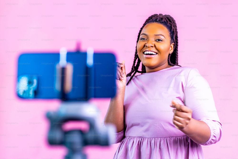 Femme à la peau foncée riant et photographiant des histoires de médias sociaux sur fond de mur rose.