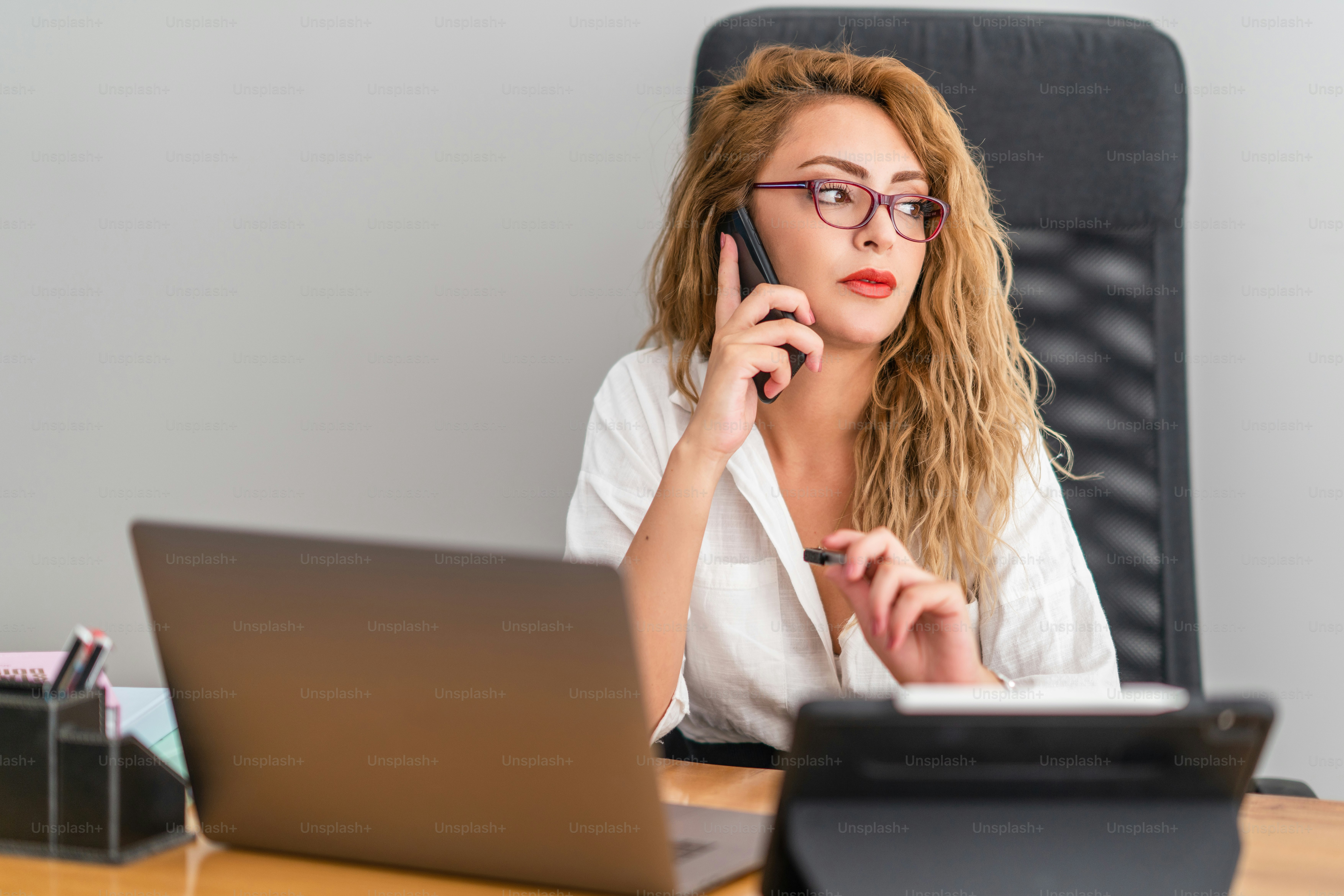 La giovane bella donna d'affari parla al telefono e siede fiduciosa sulla sua scrivania, per controllare il suo lavoro. Foto di alta qualità