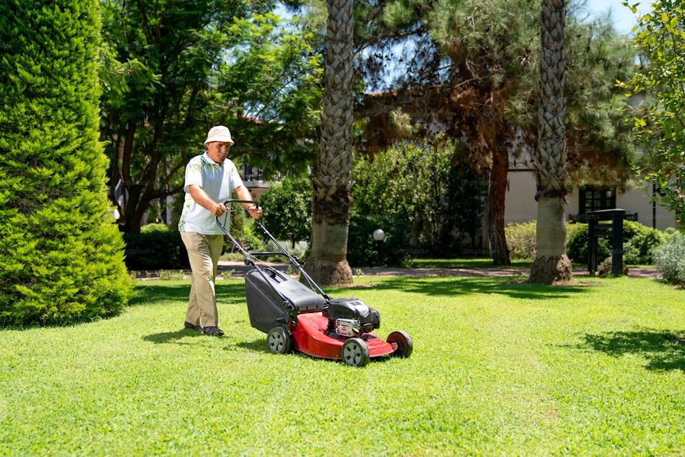 Old gardener with lawn mower in green garden