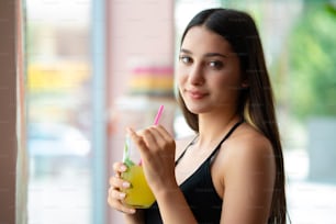 Mulher jovem sorrindo e bebendo alguma bebida na frente da janela. Foto de alta qualidade
