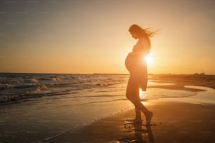 Silhueta da mulher grávida na praia no pôr do sol do mar
