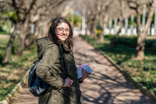 Intellectual young girl stays and look to someone in a park with some books in her hands. High quality photo