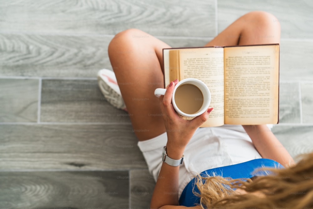 Una joven intelectual se sienta en el suelo y bebe una taza de café, mientras lee un libro. Foto de alta calidad