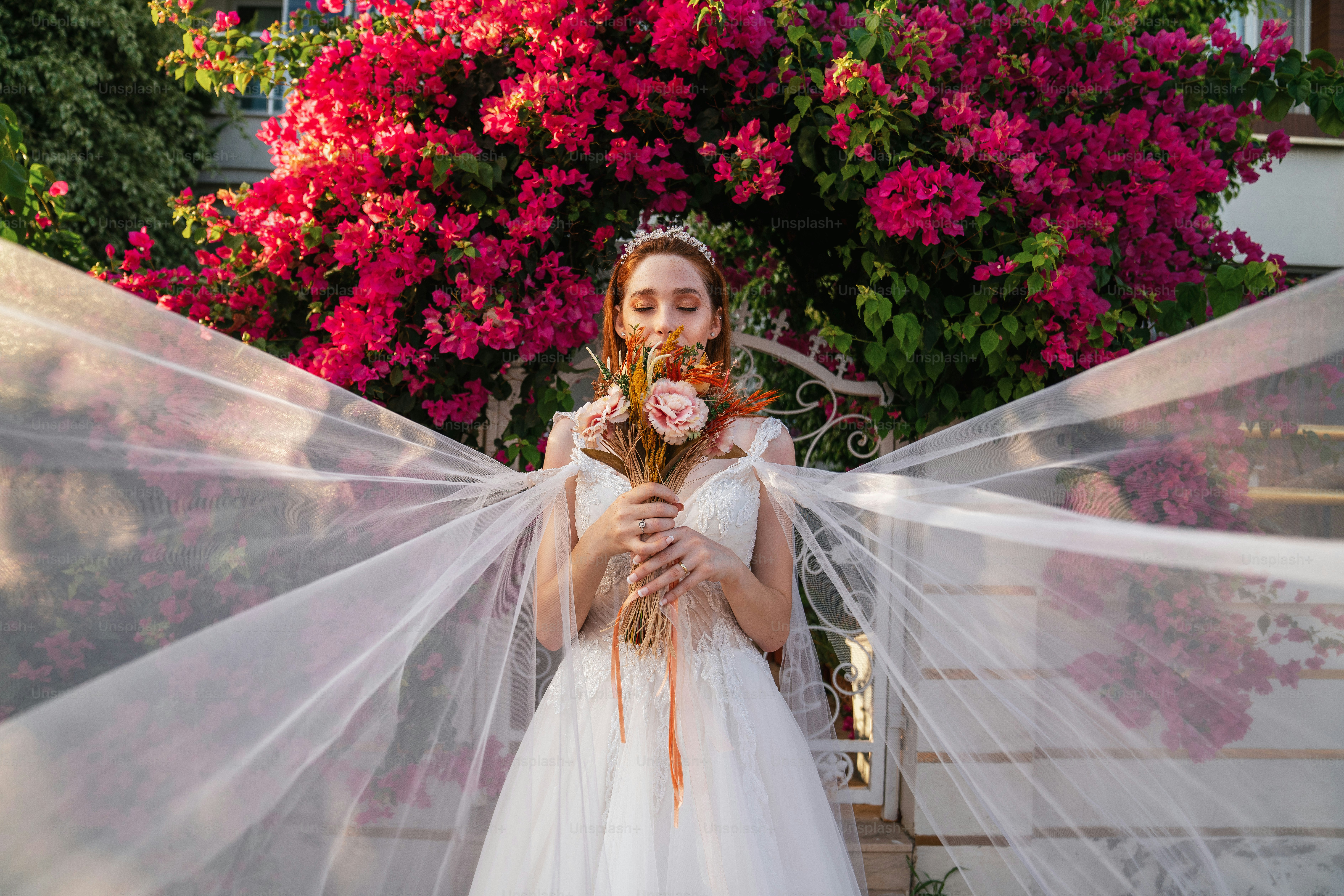 Mariée avec robe de mariée blanche tenant un bouquet de mariée coloré et séché avec fond de bougainvilliers rouges. . Photo de haute qualité