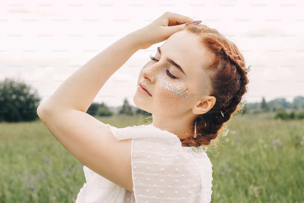 Close up portrait of young gorgeous caucasian ginger woman with freckles and sequins in field.