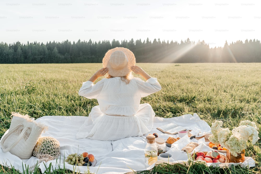 Woman in hat rear view, picnic in field. White dress, copy space.