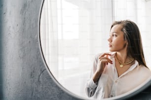 Silver bijouterie chain with pendant on woman neck. Reflection woman in the mirror, window background.