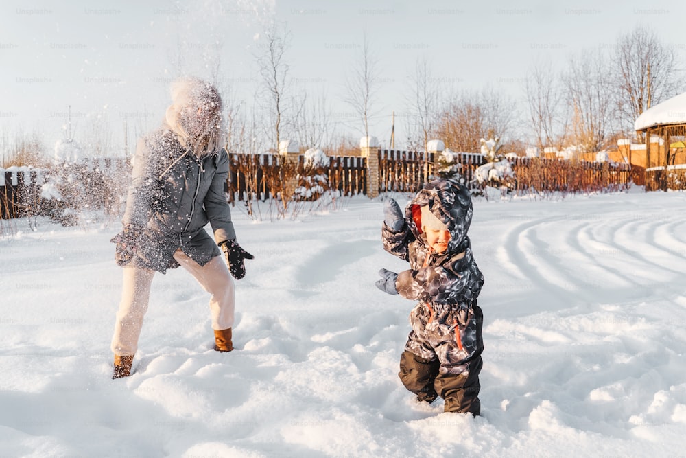 Happy mother and child throw snow and smiling. Winter walk and play.