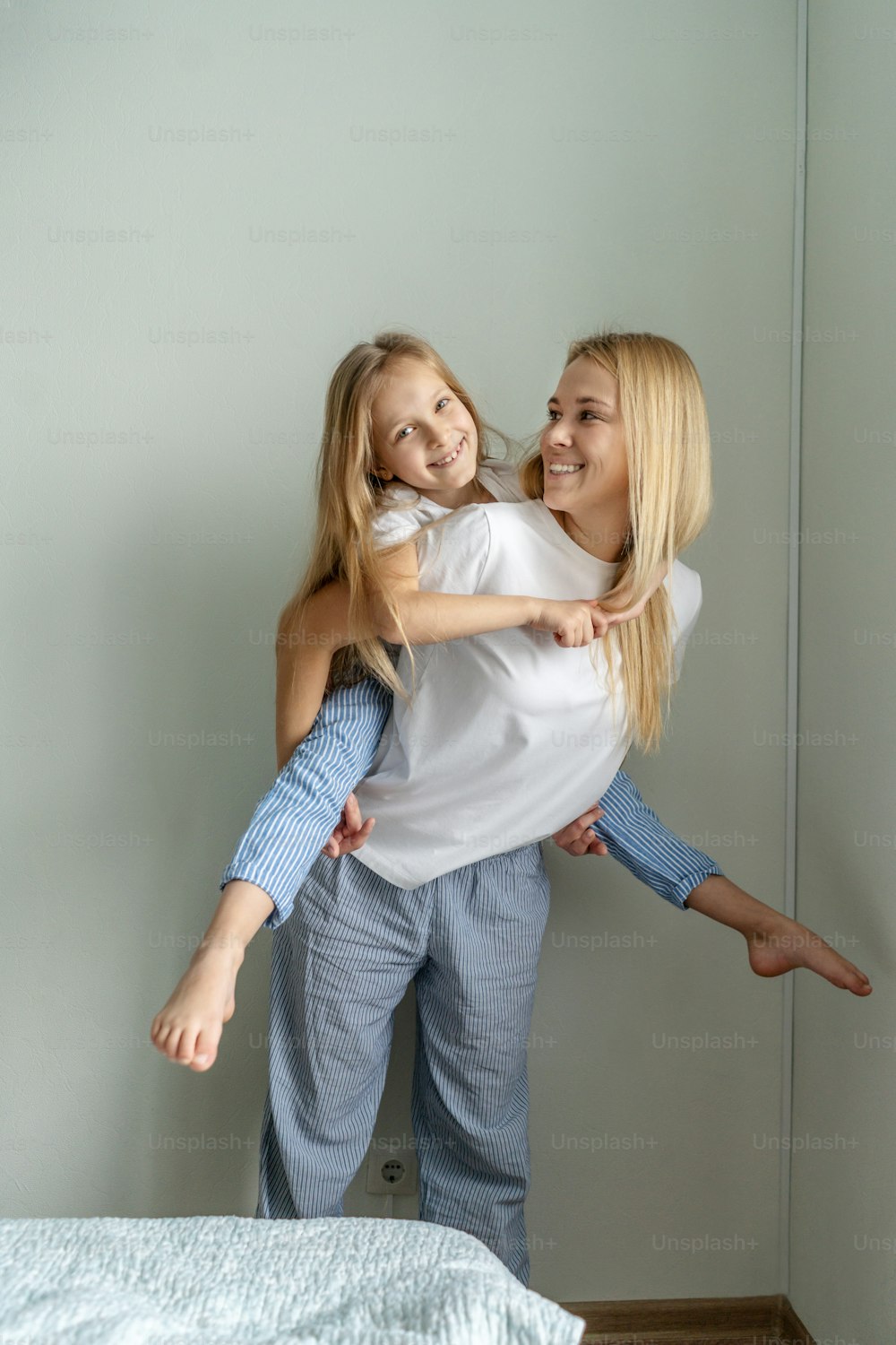 어린 소녀와 함께 엄마는 집에서 즐거운 시간을 보낸다. 가벼운 인물 사진, 흰색 티쇼츠.