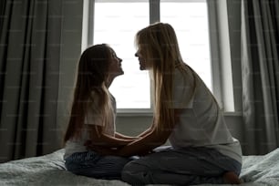 Mom with little girl in bed, silhouette. Window on background.