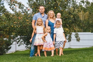 Feliz familia numerosa con niños en jardín, manzano de fondo.