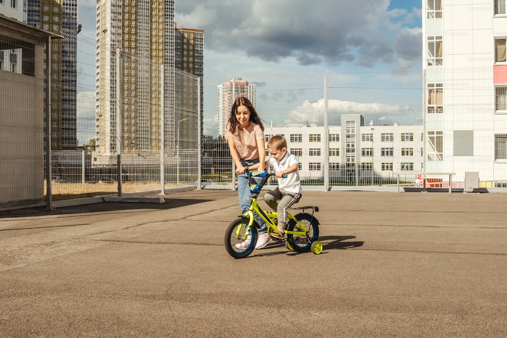 boy rides a bike with his mother. Houses on background, summer.
