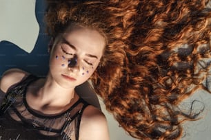 Close up portrait of young ginger curly girl with blue flowers as freckles above. Top view.