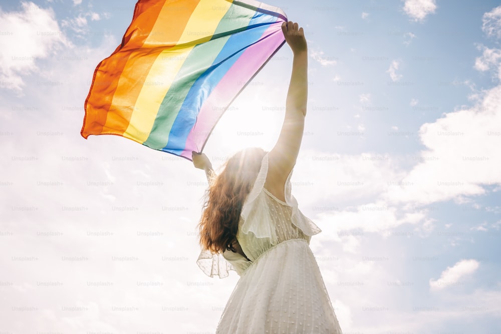 Mujer lesbiana con bandera del arco iris en el cielo de fondo. Concepto LGBTQ.