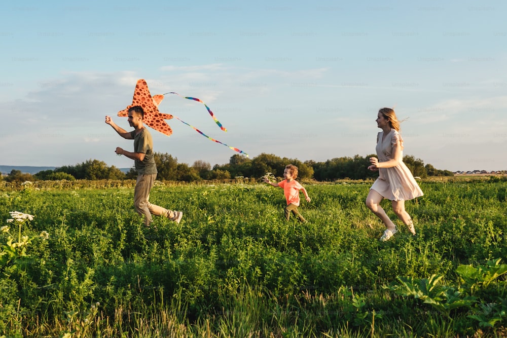 Young happy family with little boy run in field and flying a kite. Front view.